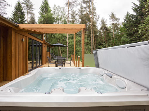 Bubbling outdoor hot tub overlooking decking area surriunded by pine trees