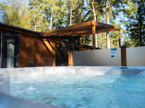 Bubbling outdoor hot tub overlooking decking area surriunded by pine trees