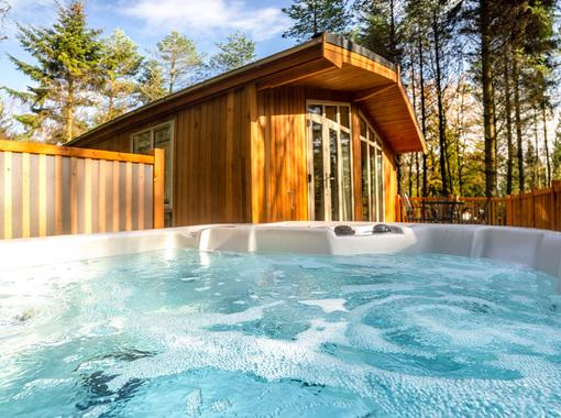 Looking out of a bubbling hot tub towards the modern lodge with pine trees in the distance