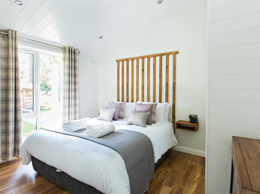 Sumptuous double bed with crisp white bedding and grey runner at the foot of bed, with full length windows