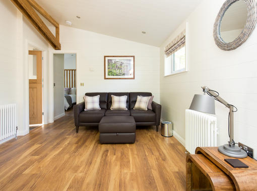 Living space with oak coloured wooden floors and comfortable brown leather sofa and footstool