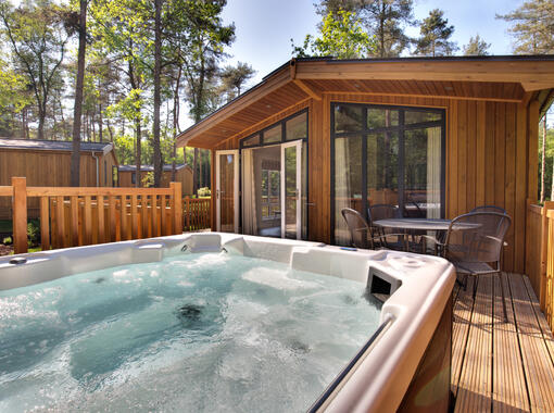 Lodge set within pine trees with beautiful blue sky, doors from lodge open onto verandah with out door hot tub