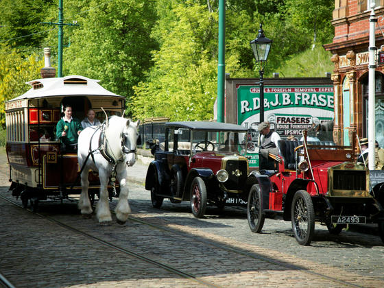 Horse drawn tram travelling past vintage cars