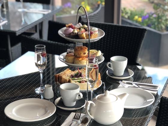 Afternoon tea on 3 tiered plates includes sandwiches, scones and sweet treats, with tea pot and glass of prosecco