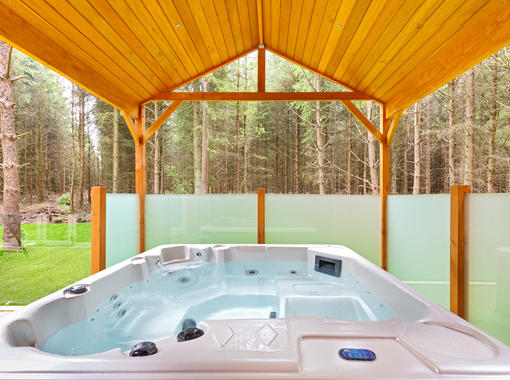 Outdoor hot tub under wooden canopy looking out on to surrounding woodland