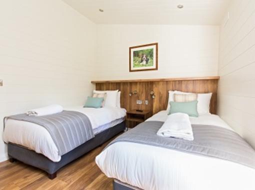 Twin beds with crisp white bedding and grey foot runner, feature wooden bed head 