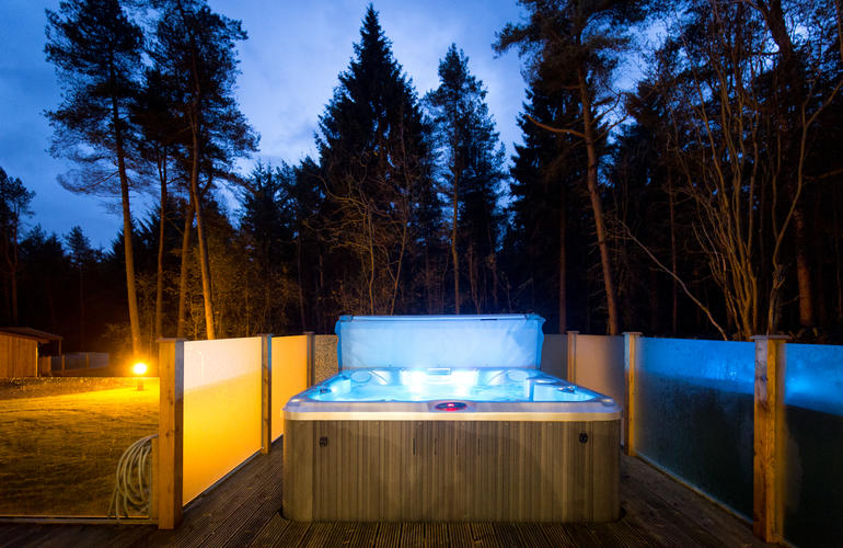 Hot tub at nigh twith lights glowing in the hot tub and surrounded  by trees